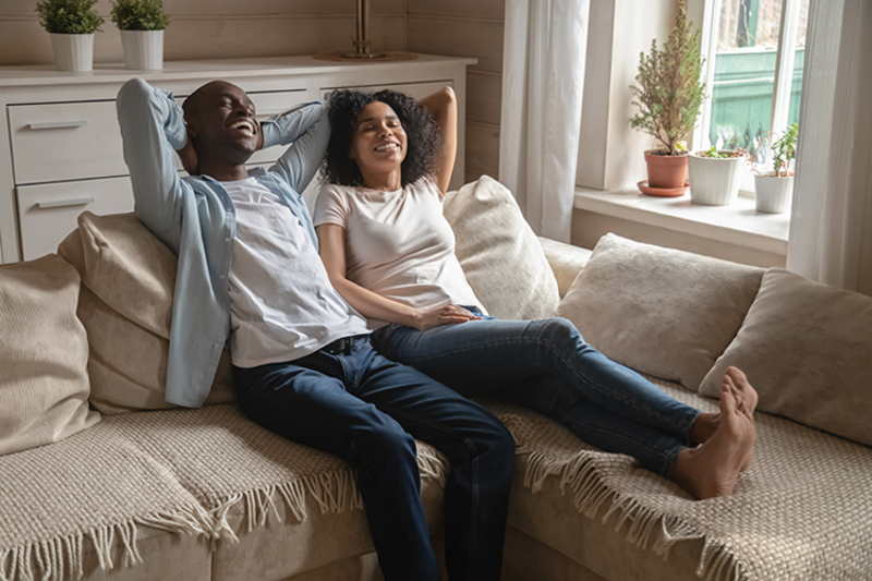 a couple sitting on their couch, taking in a deep breath of fresh air, looking relaxed and comfortable.